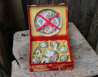 May include: A red and gold Chinese tea set in a red box with a floral design. The set includes a teapot, six cups, and a saucer. The box is lined with red satin.
