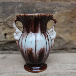May include: A small, brown and white ceramic vase with two handles. The vase has a fluted design and a glossy finish.