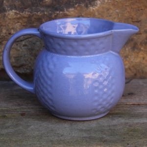 Puede incluir: Una pequeña jarra de cerámica azul claro con una superficie texturizada. La jarra tiene un cuerpo redondeado y un asa.