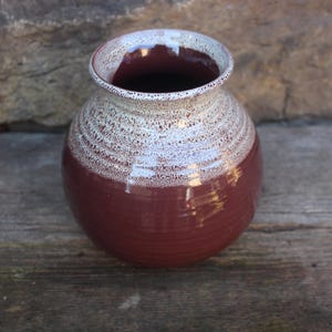 May include: A brown ceramic vase with a white glaze on the top half. The vase has a round body and a wide opening.