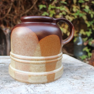 Könnte beinhalten: Eine Keramiktasse mit braunem Henkel und rundem Körper. Die Tasse hat ein zweifarbiges Design mit einem dunkelbraunen Oberteil und einer helleren braunen und beigen Basis. Die Tasse hat ein Fassungsvermögen von ca. 470 ml.