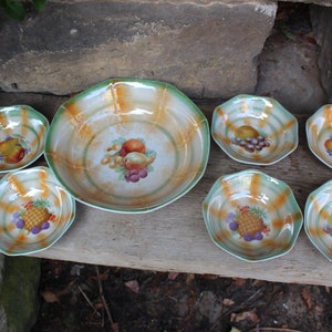 May include: A set of seven vintage porcelain bowls with a green and orange striped pattern. The bowls feature a fruit motif with a variety of fruits including pears, grapes, pineapples, and apples.