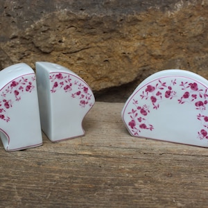 Könnte beinhalten: Ein Set aus drei weißen Salz- und Pfefferstreuern aus Keramik mit einem rosafarbenen Blumendesign. Die Streuer sind halbkreisförmig und haben einen gewellten Rand.