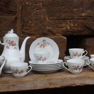 May include: A vintage tea set with a floral design. The set includes a teapot, creamer, sugar bowl, and six teacups and saucers. The teacups and saucers are stacked on top of each other.