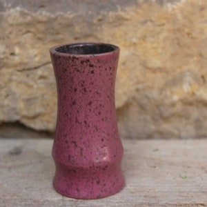 May include: A small, pink ceramic vase with a speckled finish. The vase has a narrow neck and a wide base.