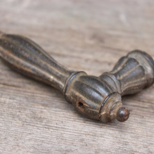 May include: A black cast iron door handle with an ornate design. The handle is in a worn condition, showing signs of age and use.