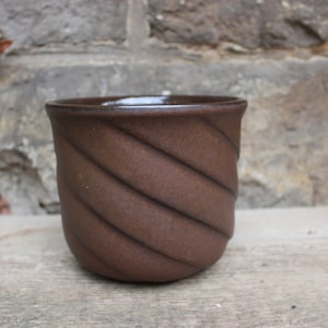 May include: A brown ceramic mug with a swirling, textured design. The mug has a smooth, glazed finish.