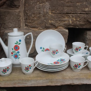 May include: A white tea set with a floral pattern in red, blue, and green. The set includes a teapot, sugar bowl, creamer, six cups, and six saucers.