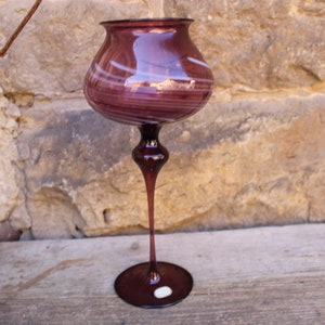 May include: A tall, clear glass vase with a purple and white swirl design. The vase has a wide, round base and a long, slender stem.