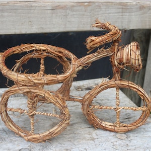 Könnte beinhalten: Ein kleines, dekoratives Fahrrad aus geflochtenen Zweigen. Das Fahrrad ist braun und hat ein verspieltes, rustikales Design.