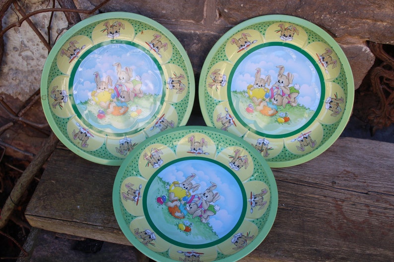 May include: Three green and yellow ceramic bowls with a bunny rabbit design. The bowls feature a blue background with three bunnies holding Easter eggs.