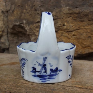 Könnte beinhalten: Ein kleiner weißer Keramikkorb mit einem blauen und weißen Windmühlenmuster. Der Korb hat einen Griff und ist mit blauen Blumenmustern verziert.
