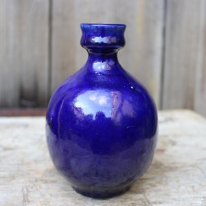 May include: A small, round, cobalt blue ceramic vase with a slightly flared opening.