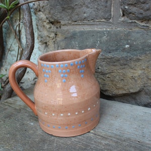May include: A terracotta pitcher with a blue and white polka dot design. The pitcher has a wide base and a rounded body.