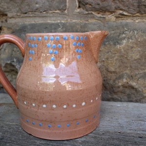 May include: A terracotta pitcher with a blue and white polka dot design. The pitcher has a wide base and a narrow spout.