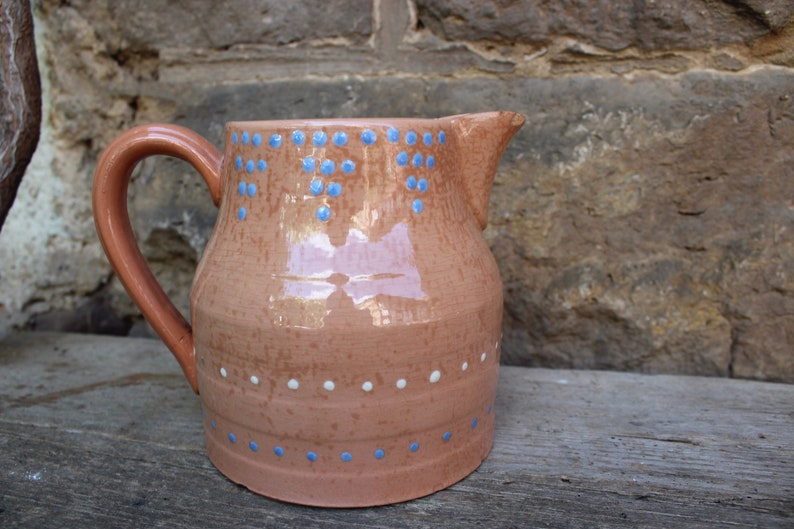 May include: A terracotta pitcher with a blue and white polka dot design. The pitcher has a wide base and a narrow spout.