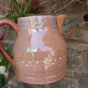 May include: A terracotta jug with a blue and white polka dot design. The jug has a wide mouth and a handle.