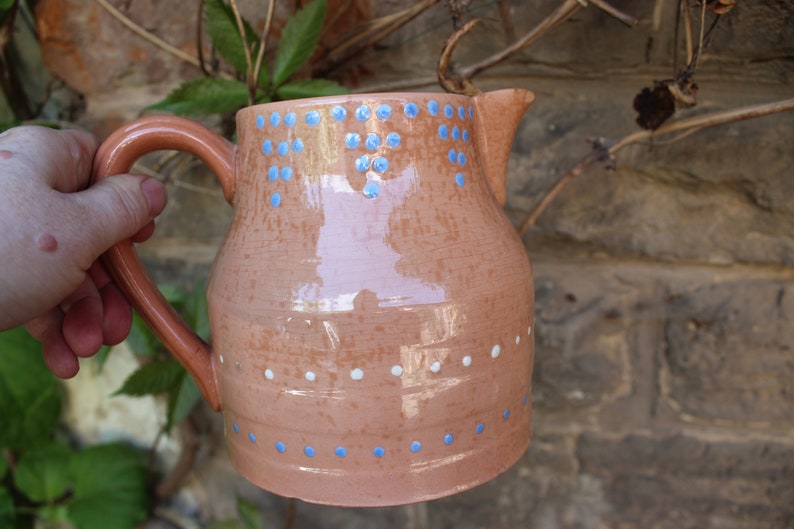 May include: A terracotta jug with a blue and white polka dot design. The jug has a wide mouth and a handle.