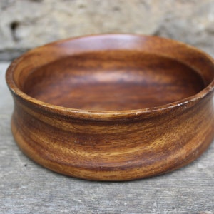 Puede incluir: Un cuenco redondo de madera de color marr&oacute;n intenso, con vetas visibles. El cuenco tiene un dise&ntilde;o ligeramente curvado y ensanchado, con un acabado liso y pulido. Adecuado para servir alimentos o como elemento decorativo, mide unos 15 cm de di&aacute;metro.