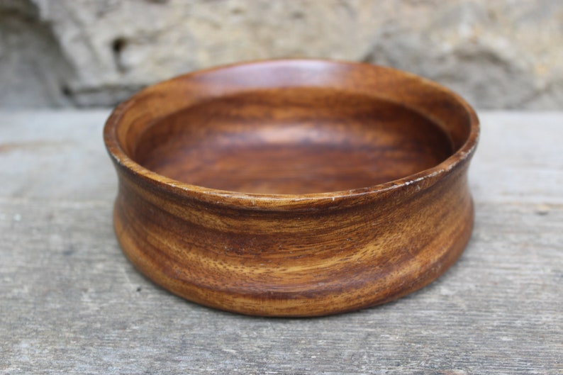 Puede incluir: Un cuenco redondo de madera de color marr&oacute;n intenso, con vetas visibles. El cuenco tiene un dise&ntilde;o ligeramente curvado y ensanchado, con un acabado liso y pulido. Adecuado para servir alimentos o como elemento decorativo, mide unos 15 cm de di&aacute;metro.