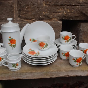 May include: A white tea set with orange floral designs. The set includes a teapot, creamer, sugar bowl, and six cups and saucers.