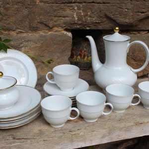 Può includere: Un set da tè in porcellana bianca con dettagli dorati. Il set comprende una teiera, una zuccheriera, un creamer e sei tazze e piattini. Il set è decorato con un delicato motivo in rilievo.