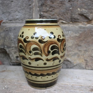 Könnte beinhalten: Eine Keramikvase mit cremefarbenem Korpus und braunen und schwarzen bemalten Blumendesigns. Die Vase hat einen runden Korpus und eine schmale Öffnung.