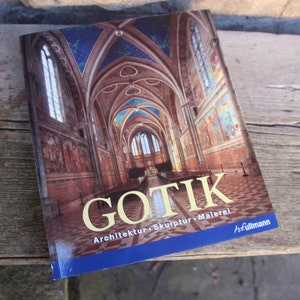 以下が含まれることがあります： 「GOTIK」というタイトルの本。青い天井とアーチ型の窓があるインテリア建築画像が特徴です。「Architektur, Skulptur, Malerei」という言葉が表紙に表示されています。本は木製の表面に置かれています。