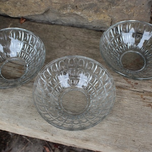 May include: Three clear glass bowls with a decorative, textured pattern. The bowls have a round shape and a centre hole.