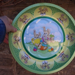 May include: A green metal serving tray with a yellow, green, and blue design featuring bunnies holding Easter eggs. The tray has a scalloped edge and is decorated with green polka dots.