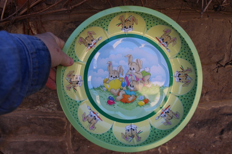 May include: A green metal serving tray with a yellow, green, and blue design featuring bunnies holding Easter eggs. The tray has a scalloped edge and is decorated with green polka dots.