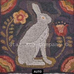May include: A white rabbit sitting in a field of flowers. The rabbit is surrounded by purple, brown, and green flowers. The background is a dark purple color. The text "Star Rug Company ©" is visible in the lower center of the image.