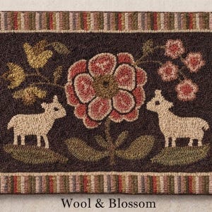 May include: A rectangular wool rug with a dark brown background features a large central flower and two sheep. The rug has a striped border in shades of brown, green, and red. The text "Wool & Blossom" is at the bottom.