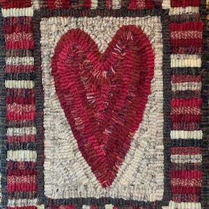 May include: A red heart rug with a white background and a multi-colored border. The border is made of stripes of red, white, black, and brown. The rug is signed "Rhonda Thomas (c)".