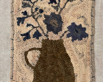 May include: A brown ceramic pitcher with a wide mouth and a handle, filled with a bouquet of blue and brown flowers. The flowers are arranged in a vase with a textured surface. The background is a light beige color.