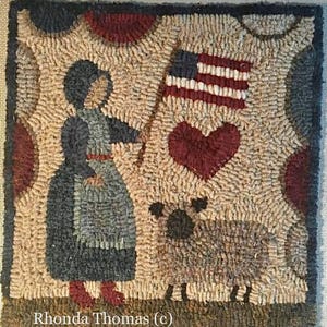May include: Hand-hooked rug featuring a colonial woman holding an American flag, a heart, and a sheep. The rug has a beige background with red, blue, and black accents. The artist's name, Rhonda Thomas, is at the bottom.