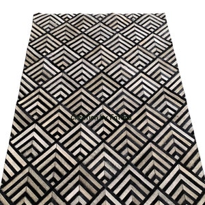 May include: Black and white geometric patterned rug made from cowhide. The rug has a diamond pattern with black and white stripes.