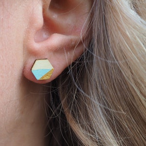 Könnte beinhalten: Ein Paar sechseckige Holzohrringe mit geometrischem Design. Die Ohrringe sind in Blautönen, Gelb und Gold bemalt.