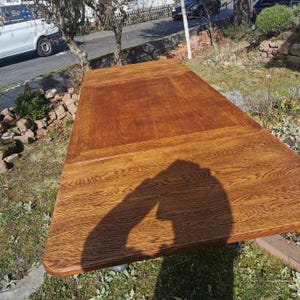 Könnte beinhalten: Ein großer, rechteckiger Esstisch aus Holz mit brauner Oberfläche. Der Tisch ist aus massivem Holz und hat eine natürliche Maserung. Der Tisch ist ausgezogen und es fällt ein Schatten auf die Oberfläche.
