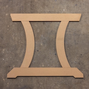 May include: A cardboard cutout of a table base with two curved supports. The base is made of brown cardboard and has a simple design.