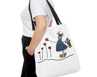 May include: White tote bag with black handles featuring a hand-drawn illustration of a girl in a blue and white polka dot dress holding a bucket with a red heart. The girl is surrounded by red hearts on stems. The text "manuela" is written in black below the illustration.