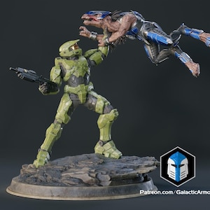 Puede incluir: Estatua detallada de una figura verde blindada que sostiene a una criatura alienígena azul y marrón. La figura sostiene un arma. La base es un terreno rocoso. El logotipo de Galactic Armory está en la esquina inferior derecha.