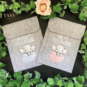 May include: Two grey felt book covers with embroidered elephants. One cover has a blue elephant and the text "Matthew's Little Red Book". The other cover has a pink elephant and the text "Emily's Little Red Book".