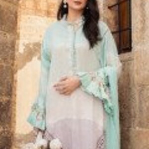 Puede incluir: Una t&uacute;nica de manga larga azul claro y blanca con un dobladillo con volantes y mangas con volantes. La t&uacute;nica tiene un frente abotonado y un estampado floral. La modelo lleva pantalones blancos y sostiene un ramo de flores blancas.