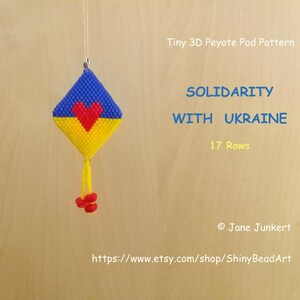 Könnte beinhalten: Ein kleines 3D-Peyote-Pod-Muster-Perlenprojekt in den Farben Blau, Gelb und Rot. Das Projekt ist in Form eines Drachens mit einem Herz in der Mitte gestaltet. Der Text "Solidarität mit der Ukraine" und "17 Reihen" wird über dem Projekt angezeigt. Der Text "© Jane Junckert" und "https://www.etsy.com/shop/ShinyBeadArt" wird unter dem Projekt angezeigt.