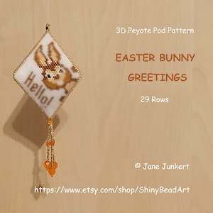 May include: A 3D peyote pod pattern for an Easter bunny greeting. The pattern is 29 rows and features a bunny with the word "Hello!" on a white background. The pattern is shown hanging from a gold string with orange beads.