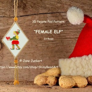 May include: A 3D peyote pod pattern for a female elf ornament. The pattern is 23 rows and features a green and red elf with a white background. The pattern is displayed on a white diamond-shaped piece of paper with a gold tassel.