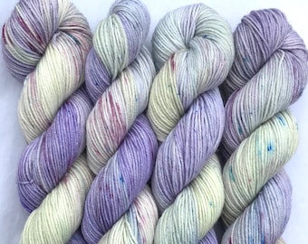 May include: Three skeins of hand-dyed yarn in a light purple and cream colorway with speckles of color throughout.