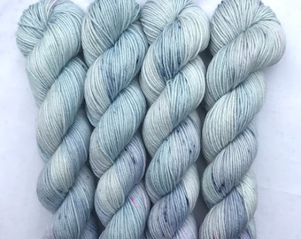 May include: Four skeins of light blue yarn with flecks of white, pink, and purple. The yarn is arranged in a spiral pattern.