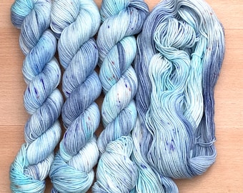 May include: Four skeins of blue and white speckled yarn with a subtle color gradient. The yarn is soft and fluffy, perfect for knitting or crocheting.